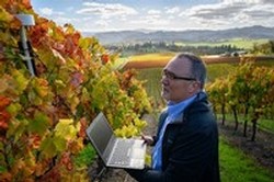 Greg Jones in the vineyard overlooking Abacela Winery, holding a laptop and downloading data