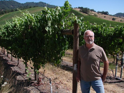 Earl Jones, founder, standing in front of a fully mature grapvine with a lush vineyard in the background.